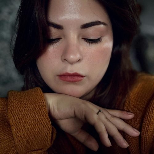 Close-up portrait of a young woman with closed eyes, wearing a warm brown sweater, in a serene and relaxed pose.